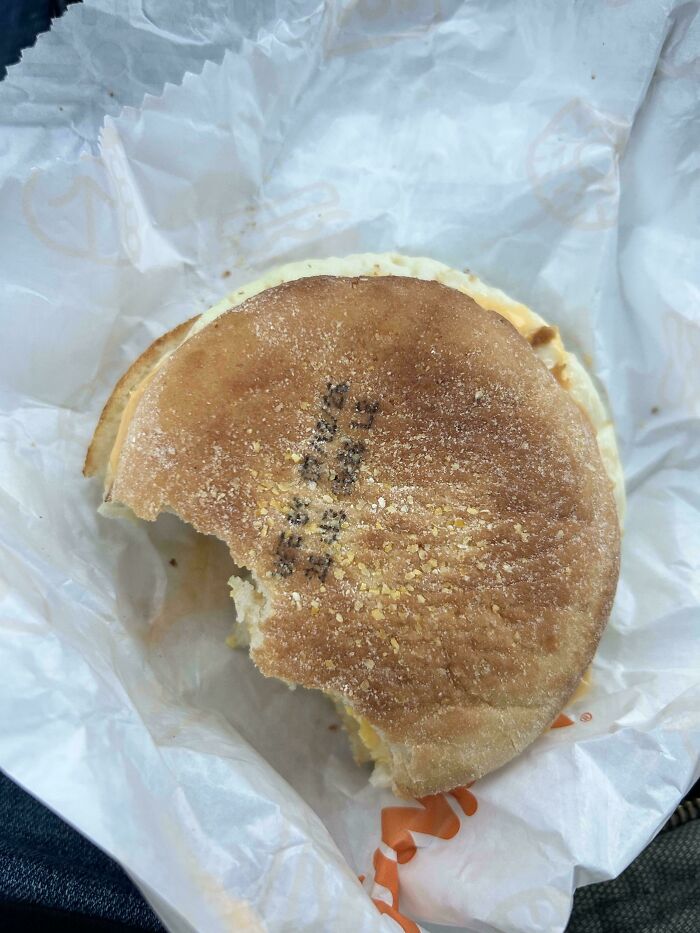 A half-eaten breakfast sandwich with a strange black stamp on the bun, a weird and unexpected moment of the day.