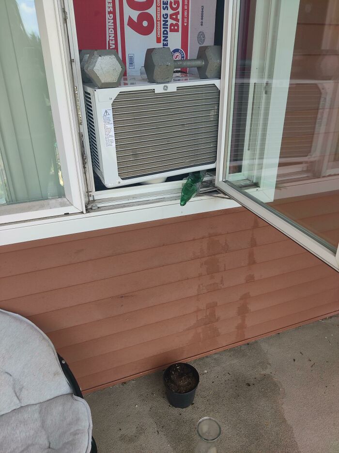 A hilariously bad DIY example of an AC unit precariously propped in a window with weights and cardboard, demonstrating a poor attempt to fix it.
