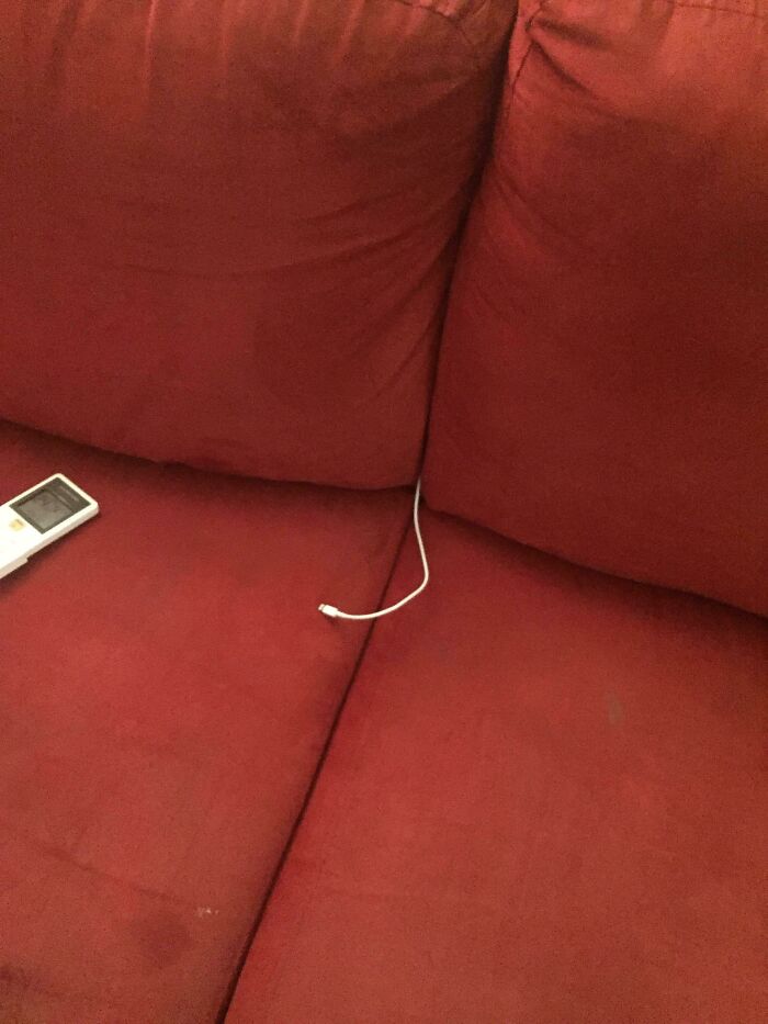 A hilariously bad example of DIY: a charging cable disappearing into the crevice of a red couch, highlighting a DIY charging solution.
