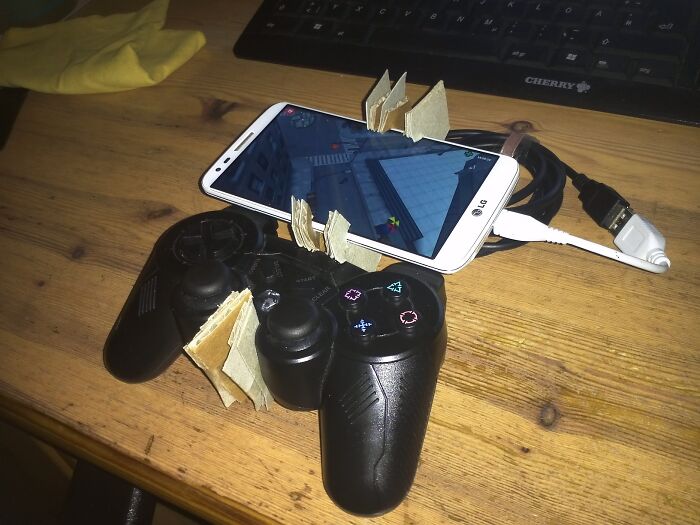 A hilariously bad example of DIY: a smartphone propped up with cardboard on a game controller, demonstrating a DIY gaming setup.