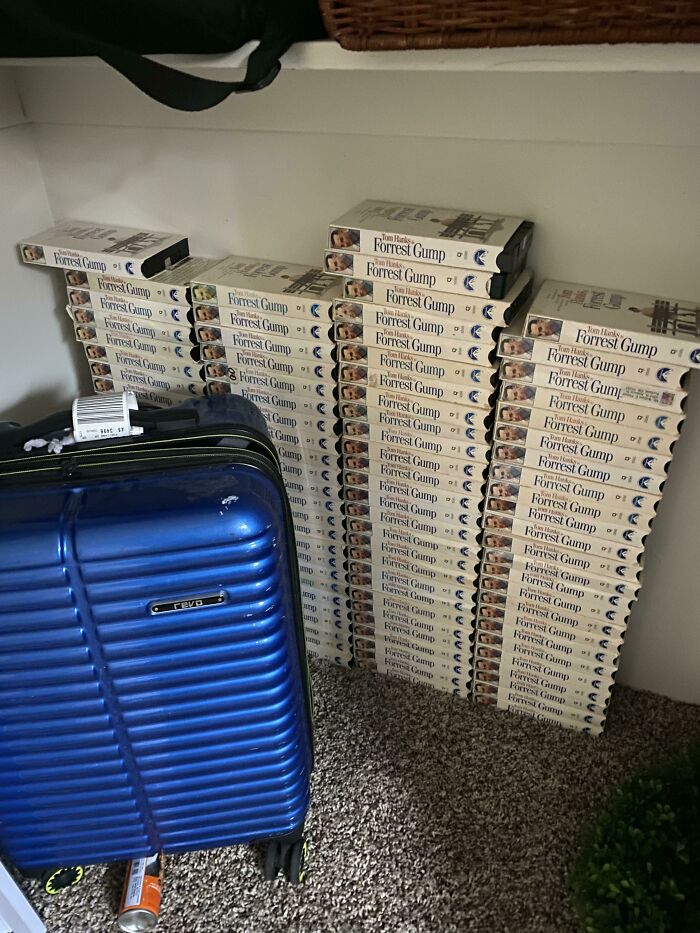 Numerous Forrest Gump VHS tapes stacked beside a blue suitcase, a weird and interesting moment.