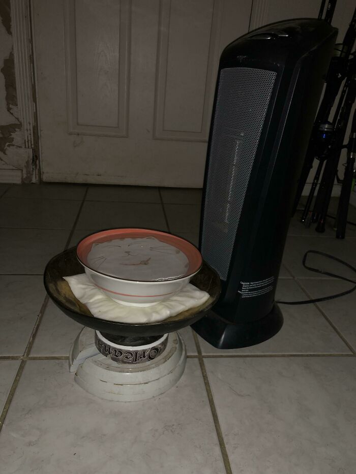 Hilariously bad DIY: a bowl of liquid placed on an improvised stand next to a tall, black electric heater on a tiled floor.