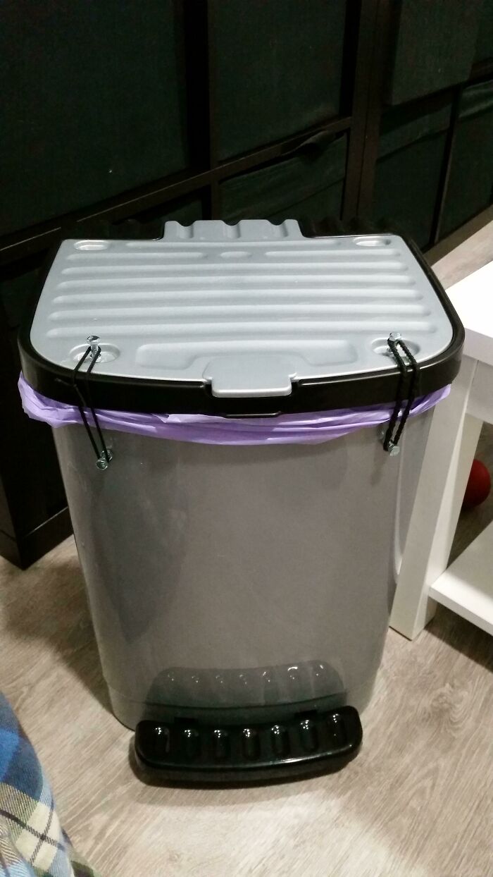 Hilariously bad DIY: a gray trash can with a purple trash bag secured by rubber bands to the lid, showcasing a DIY fix.