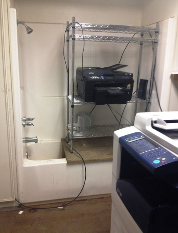 Hilariously bad DIY: a printer and electronic devices on a metal shelf next to a bathtub and shower in a bathroom.