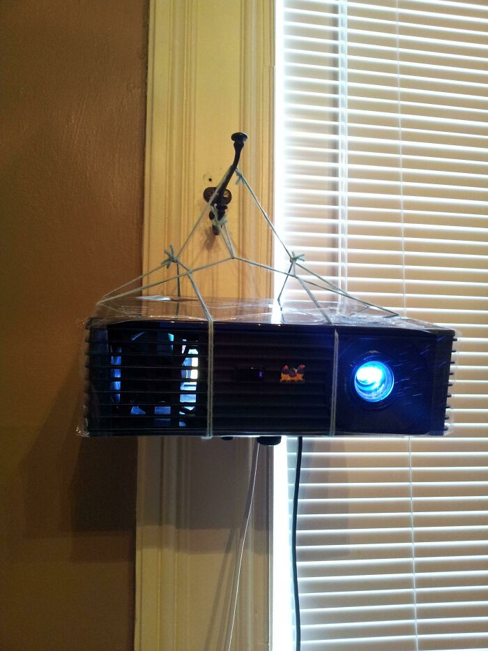 Hilariously bad DIY: A projector precariously hung from a doorframe with string and plastic wrap, next to blinds.