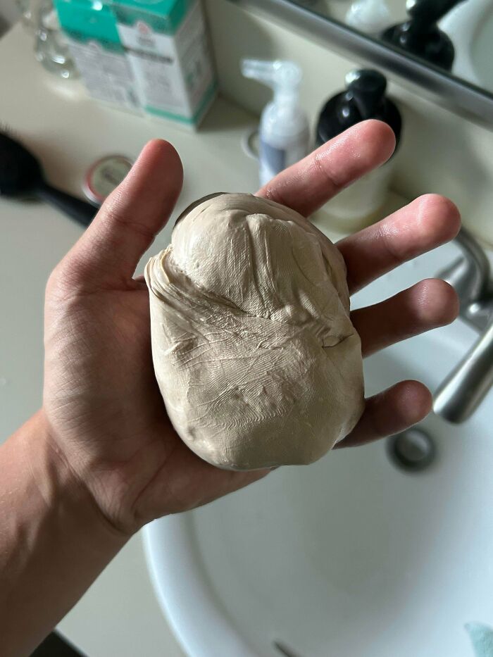 A hand holding a blob of putty or clay, resembling a human organ, showcasing a weird and unexpected moment.