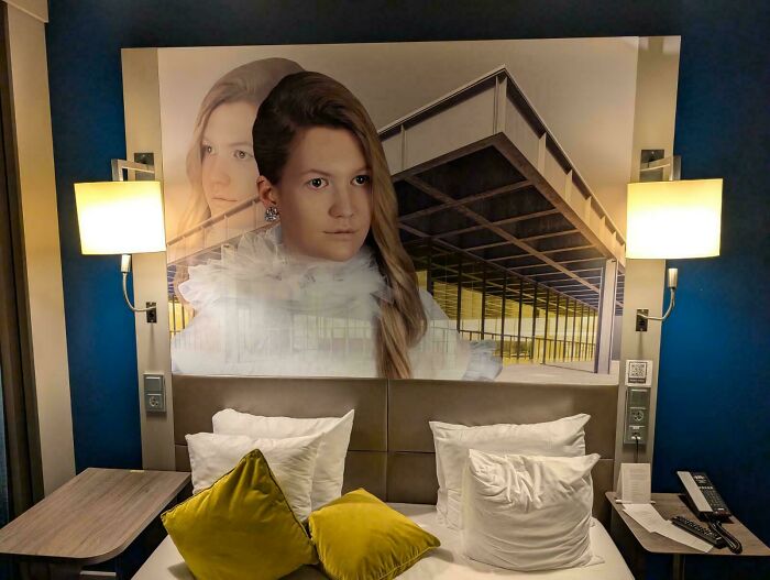 A hotel room bed with a large, artistic headboard featuring a woman's face and a modern building, a weird and unexpected moment.
