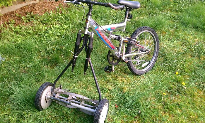 A hilariously bad DIY lawnmower made from a bicycle, standing in a grassy yard.