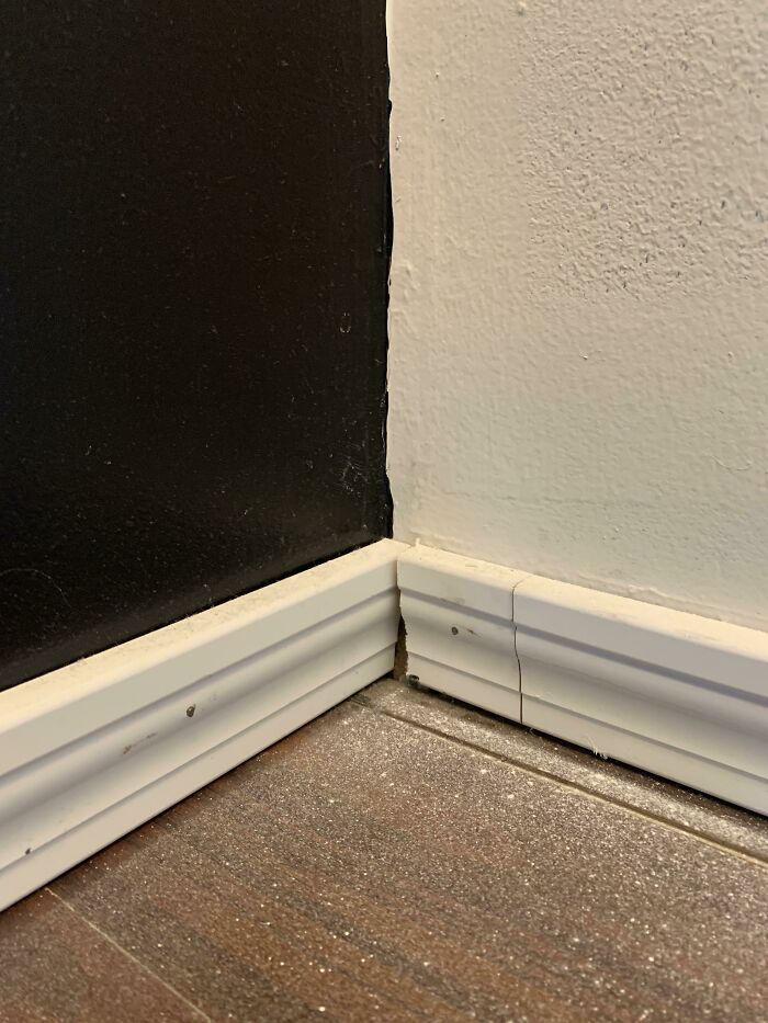 Hilariously bad DIY baseboard installation with gaps and uneven cuts at a wall corner.