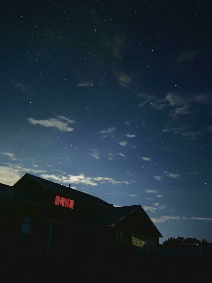 A dark house with a single red-lit window, silhouetted against a starry night sky, creating an interesting moment.