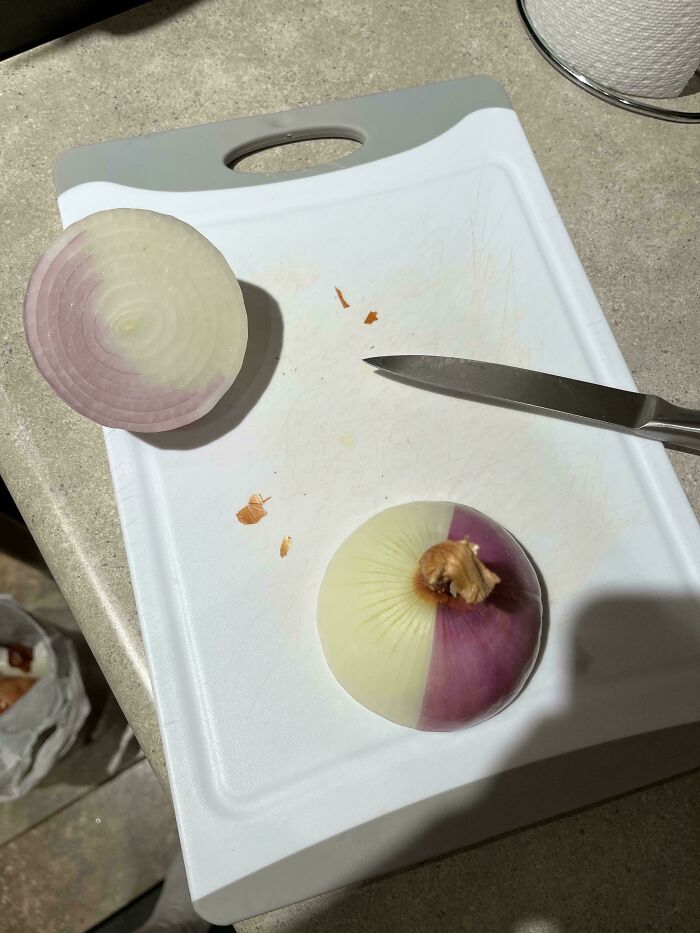 A half-white, half-purple onion on a cutting board next to a knife, an interesting and unexpected moment.