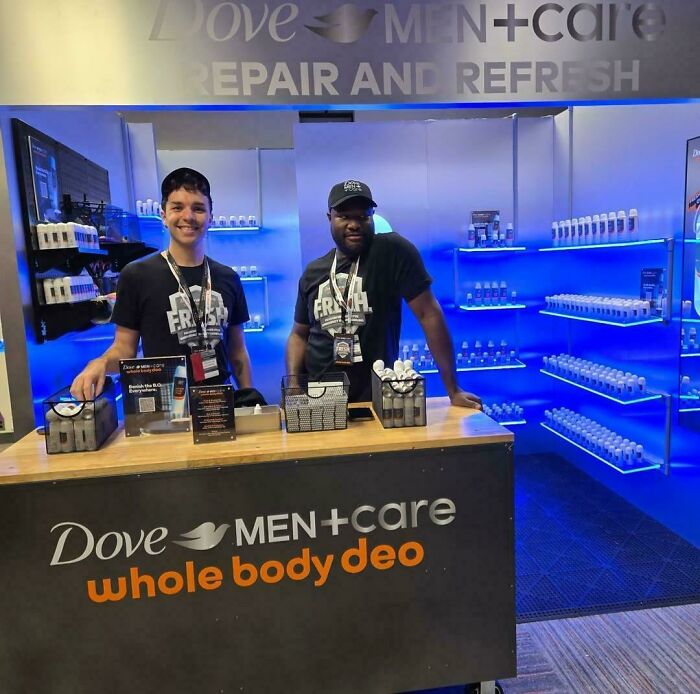 Two men smiling behind a Dove Men+Care booth, a weird and unexpected moment captured.