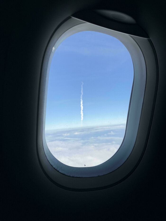 A view from an airplane window showing a contrail in the sky, an interesting and unexpected aerial sight.