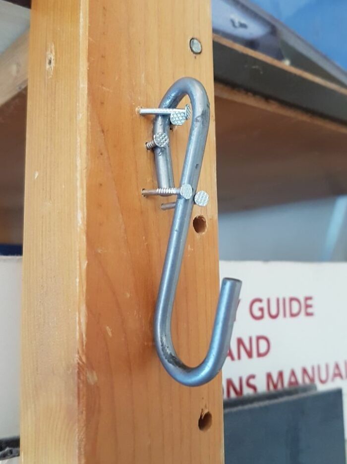 A metal S-hook nailed precariously to a wooden beam, a bad example of DIY work.