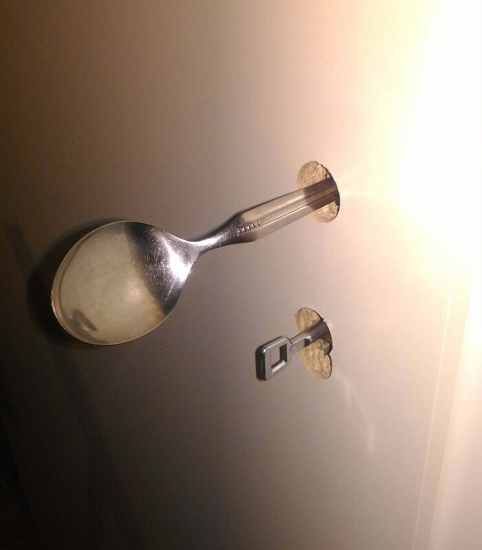 A spoon and a key used as hilariously bad DIY wall hooks, hammered into the wall.