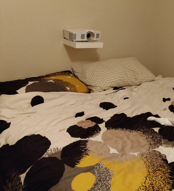 A projector placed on a small shelf above a bed, a bad example of DIY setup.