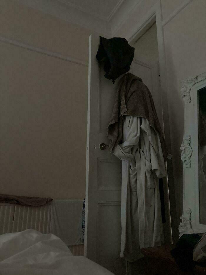 A shadowy figure of clothes hanging on a door, creating an unexpected and weird moment in a dim room.