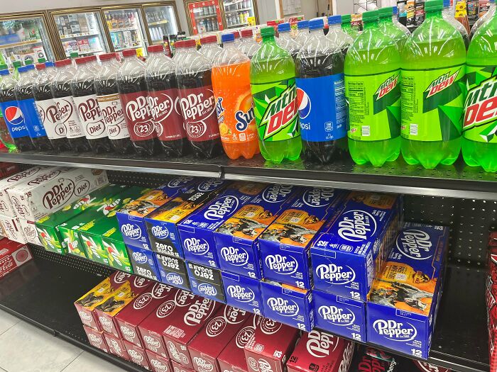 A grocery store aisle stocked with rows of Dr. Pepper and Mountain Dew sodas, an infuriating obstacle for healthy choices.