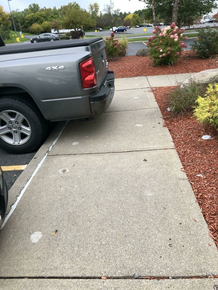 A gray pickup truck is parked over a sidewalk, creating a mildly infuriating obstacle for pedestrians.