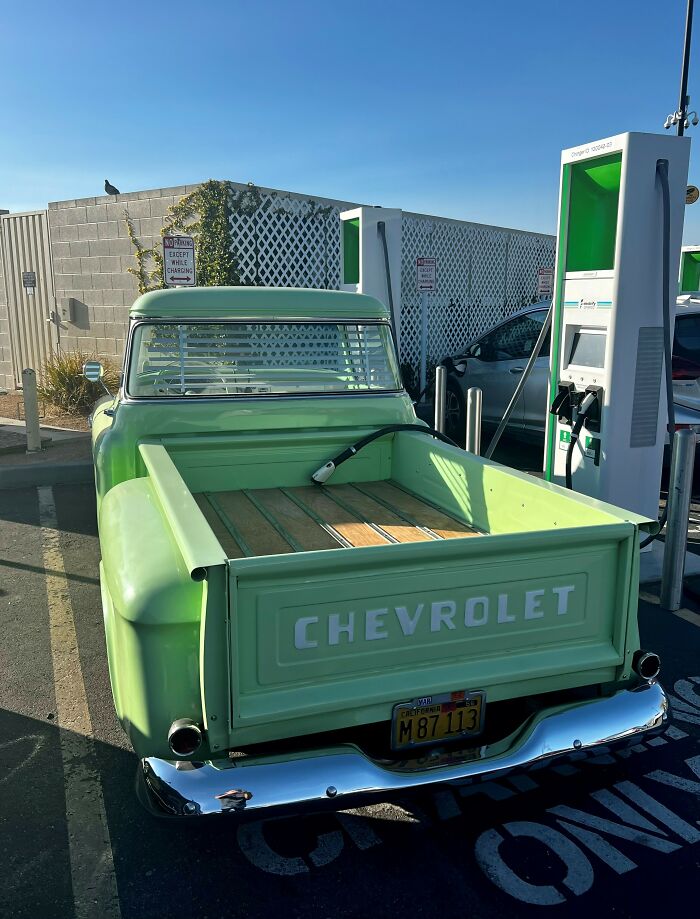 A vintage green Chevrolet truck at an EV charging station, presenting a mildly infuriating obstacle for electric vehicles.
