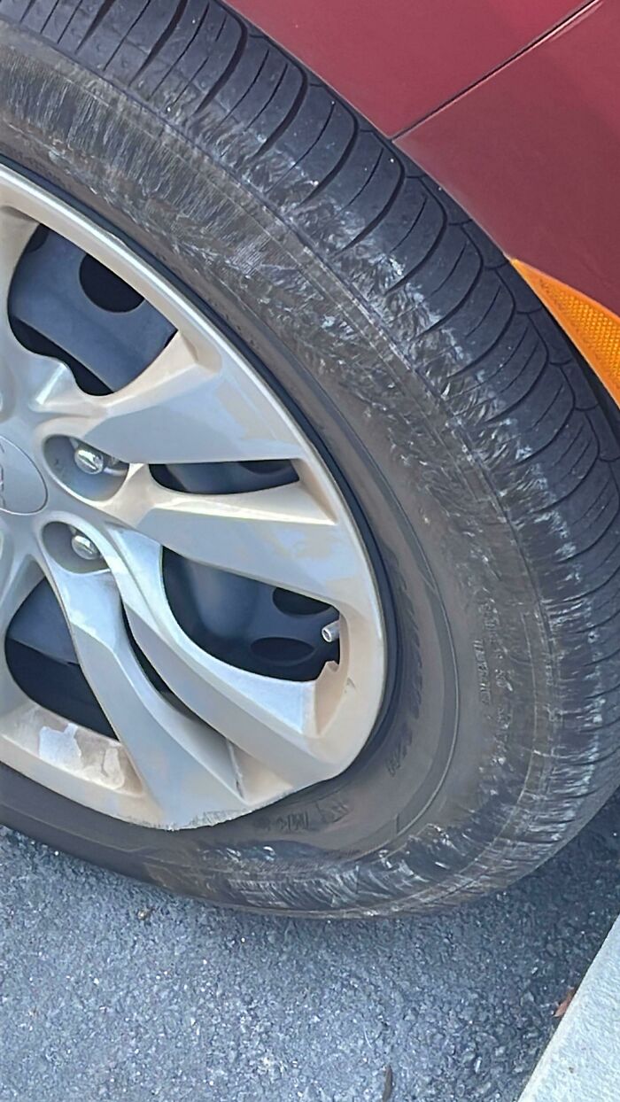 A mildly infuriating obstacle: a close-up of a flat car tire with a car jack visible behind it.