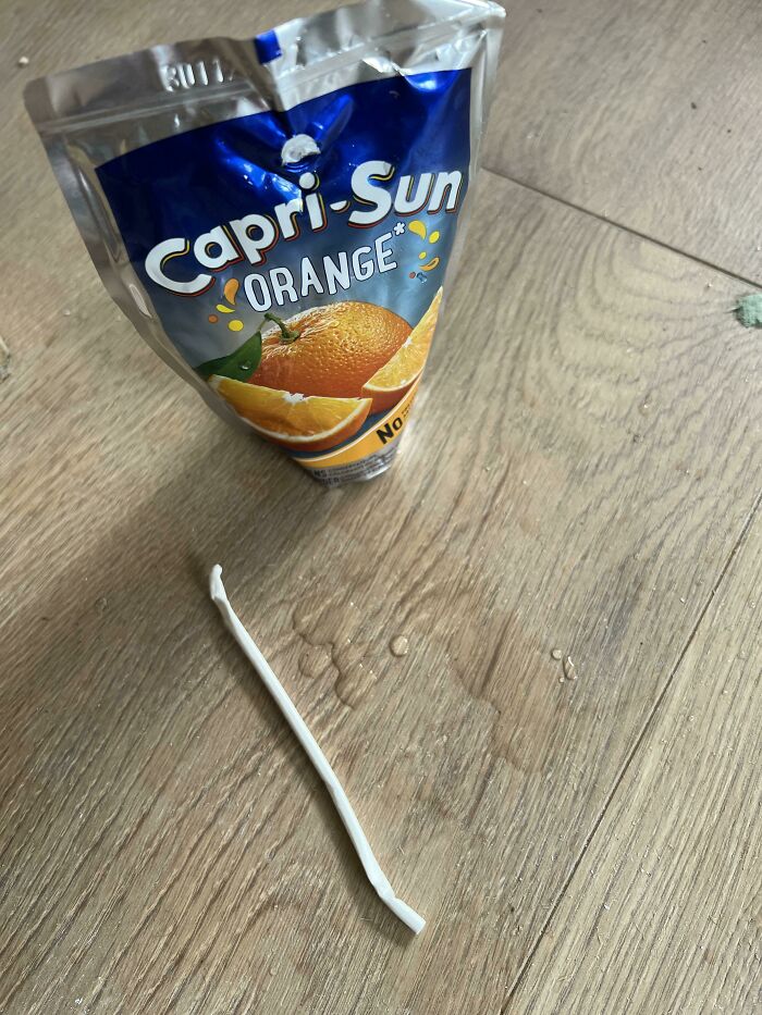 A Capri-Sun juice pouch with its straw bent and broken on a wooden floor, a mildly infuriating obstacle.