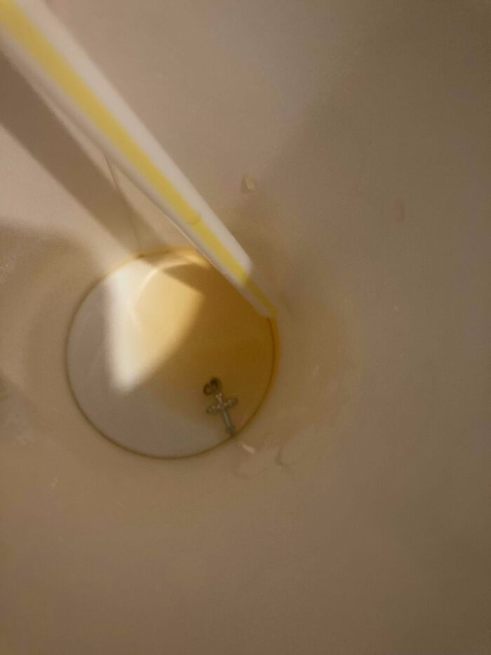 A small silver cross charm at the bottom of a drink cup, an infuriating obstacle found unexpectedly.