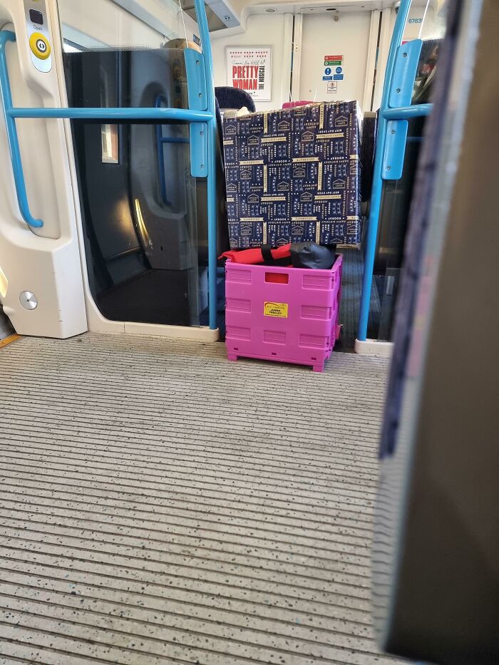 Luggage and a pink crate blocking an aisle on a train, a mildly infuriating obstacle for passengers trying to pass.