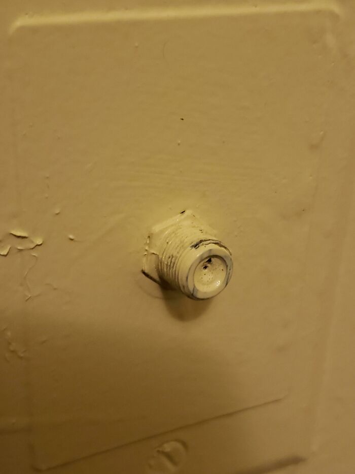 A wall-mounted threaded connector covered in paint, a mildly infuriating obstacle for intended use.