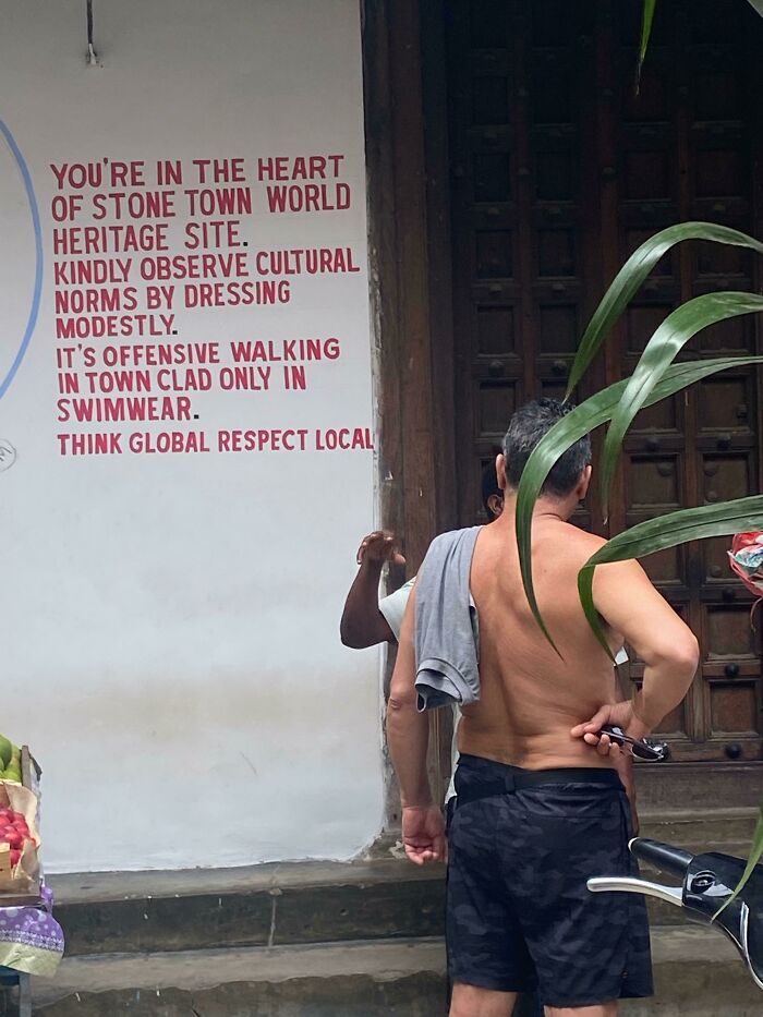 A mildly infuriating obstacle: Man standing shirtless despite a sign about cultural norms in Stone Town World Heritage Site.