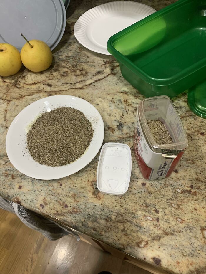 A plate overflowing with black pepper, next to an empty pepper container, a mildly infuriating obstacle.