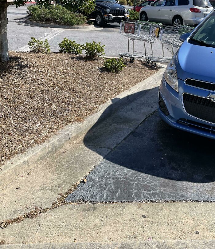 A blue car parked incorrectly with shopping carts in the background, a mildly infuriating parking obstacle.