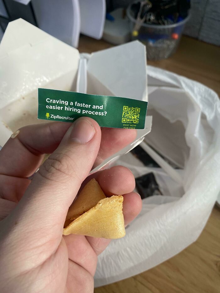 A hand holding a fortune cookie and an ad from ZipRecruiter, a mildly infuriating obstacle during a meal.