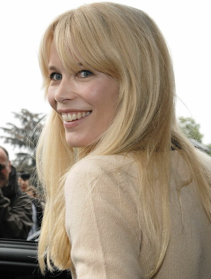 A smiling Claudia Schiffer with blonde hair and blue eyes, wearing a light-colored sweater, a highlight of her career.