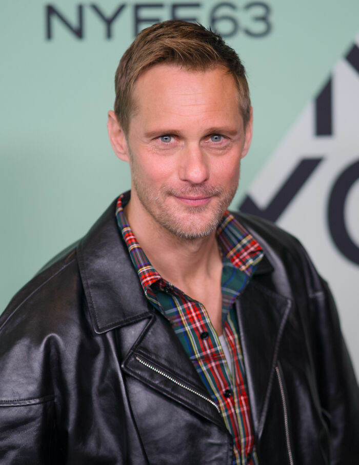 Alexander Skarsgård poses, showcasing his career highlights and bio in a black leather jacket and plaid shirt.