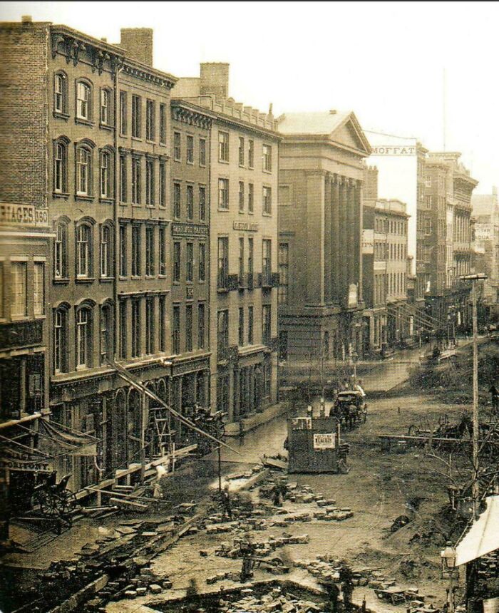 A rare photo from American history depicts a historical street scene with tall buildings and a dirt road under construction.