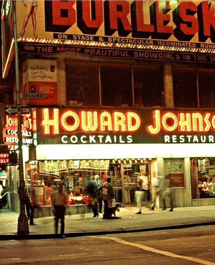A fascinating photo from American history of a lively street scene at night, featuring a Howard Johnson restaurant and a Burlesque sign.