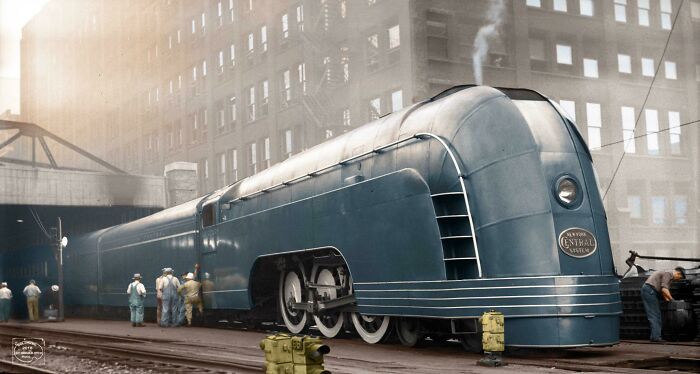Rare American History photo showing a sleek, dark train with onlookers on tracks near a building.