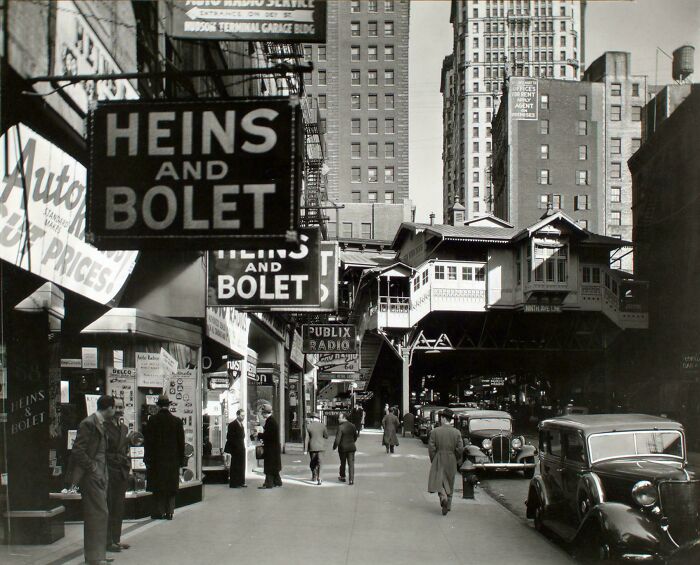 Fascinating photo of a bustling street scene with an elevated train and storefronts from American history.