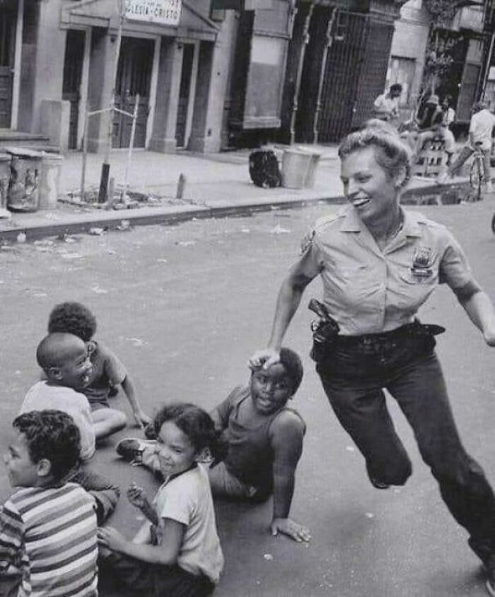 Rare photo of a police officer playfully interacting with children on a street from American history.