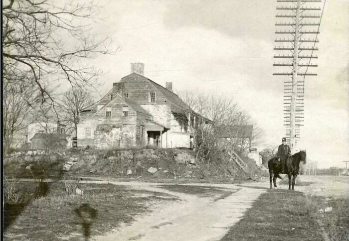 A man on horseback near an old house and telephone poles, a rare photo from American history.