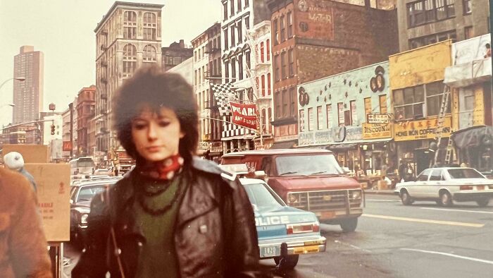 A fascinating photo from American history shows a woman with big hair on a city street with vintage cars and buildings.