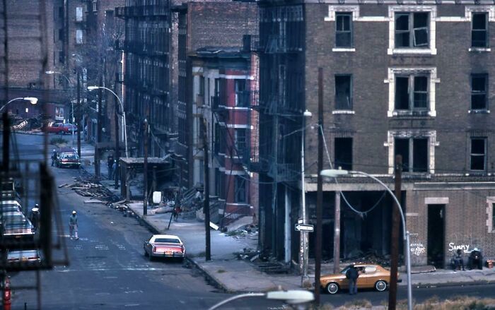 A dilapidated urban street with damaged buildings and a few cars, a fascinating photo from American history.