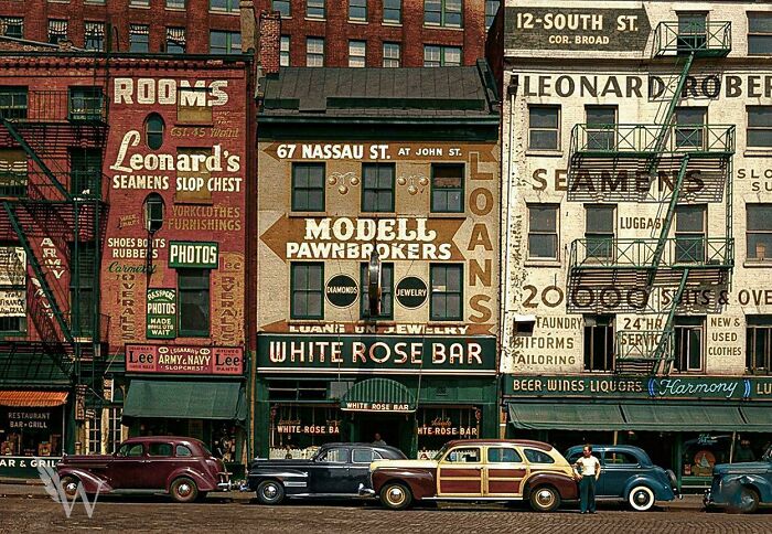 A colorful street scene with vintage cars parked in front of various shops, a fascinating photo from American history.