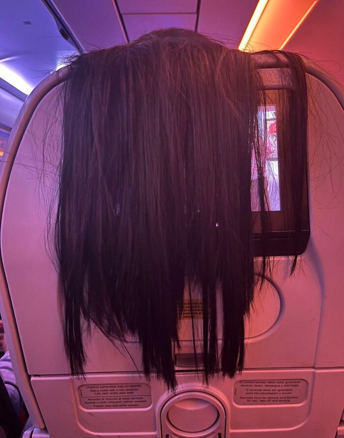 Long dark hair draped over an airplane seatback screen, a mildly infuriating obstacle for passengers.