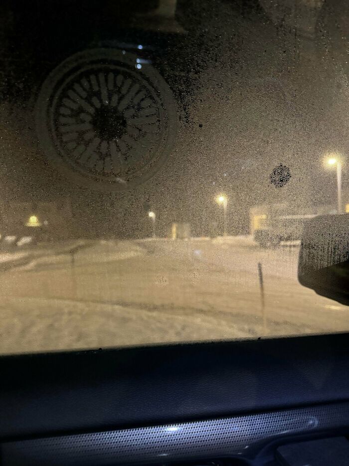 A foggy car window with a circular pattern drawn on it, looking out at a snowy landscape with streetlights, a thing people lost hope to find.