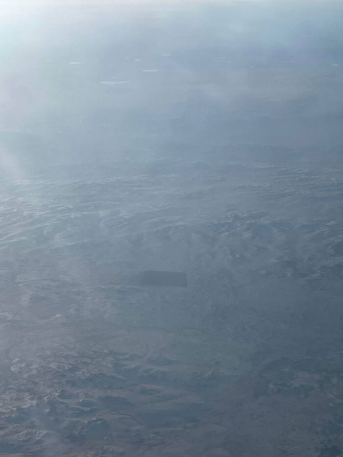Odd things on Google Maps: a mysterious, dark rectangular object seen from an airplane window over hazy mountains.