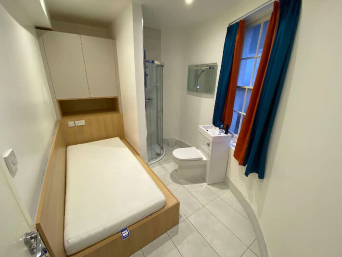 A compact Airbnb listing with a single bed, a toilet, and a shower, emphasizing a very small living area.