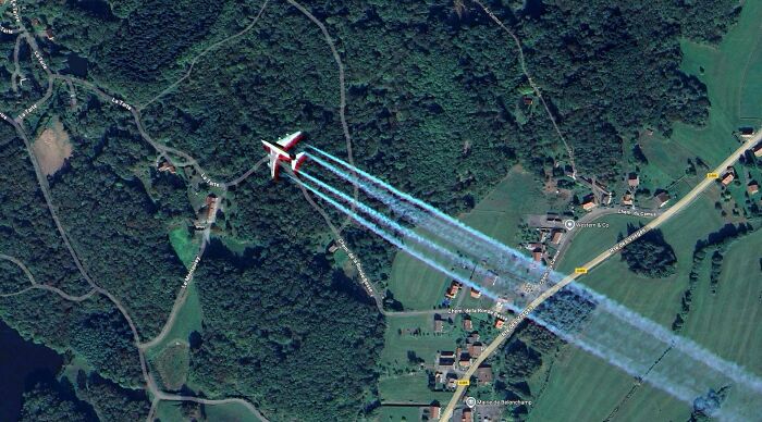 Odd things found on Google Maps: a brightly colored airplane flying over a rural landscape with contrails.