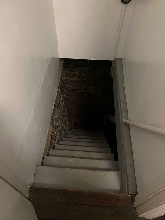 A dark, steep stairway descends into a dimly lit basement, a surprising feature in an Airbnb listing, highlighting listing surprises.